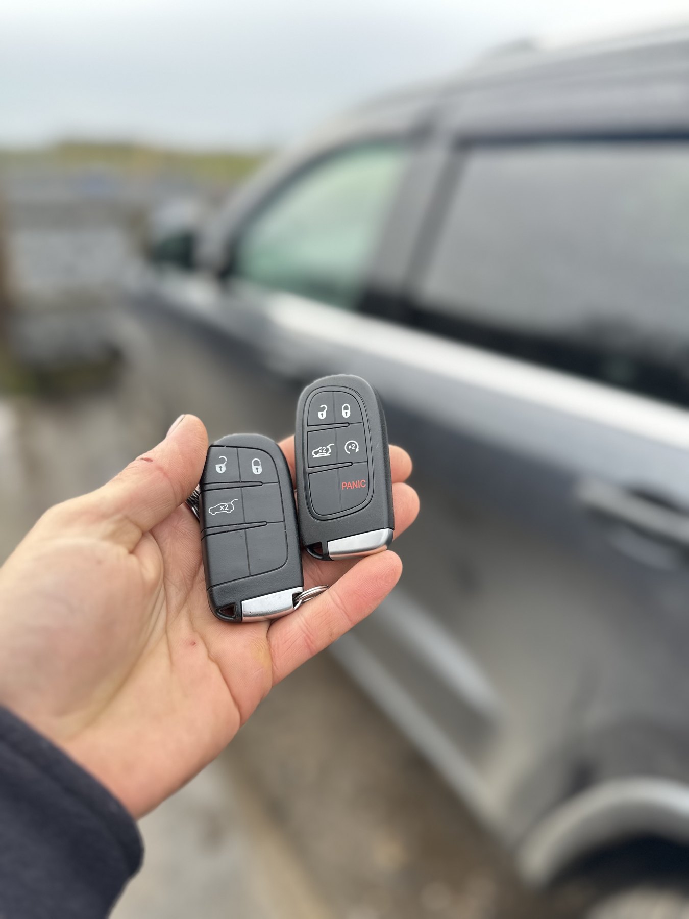 Two proximity key fobs beside a grey vehicle