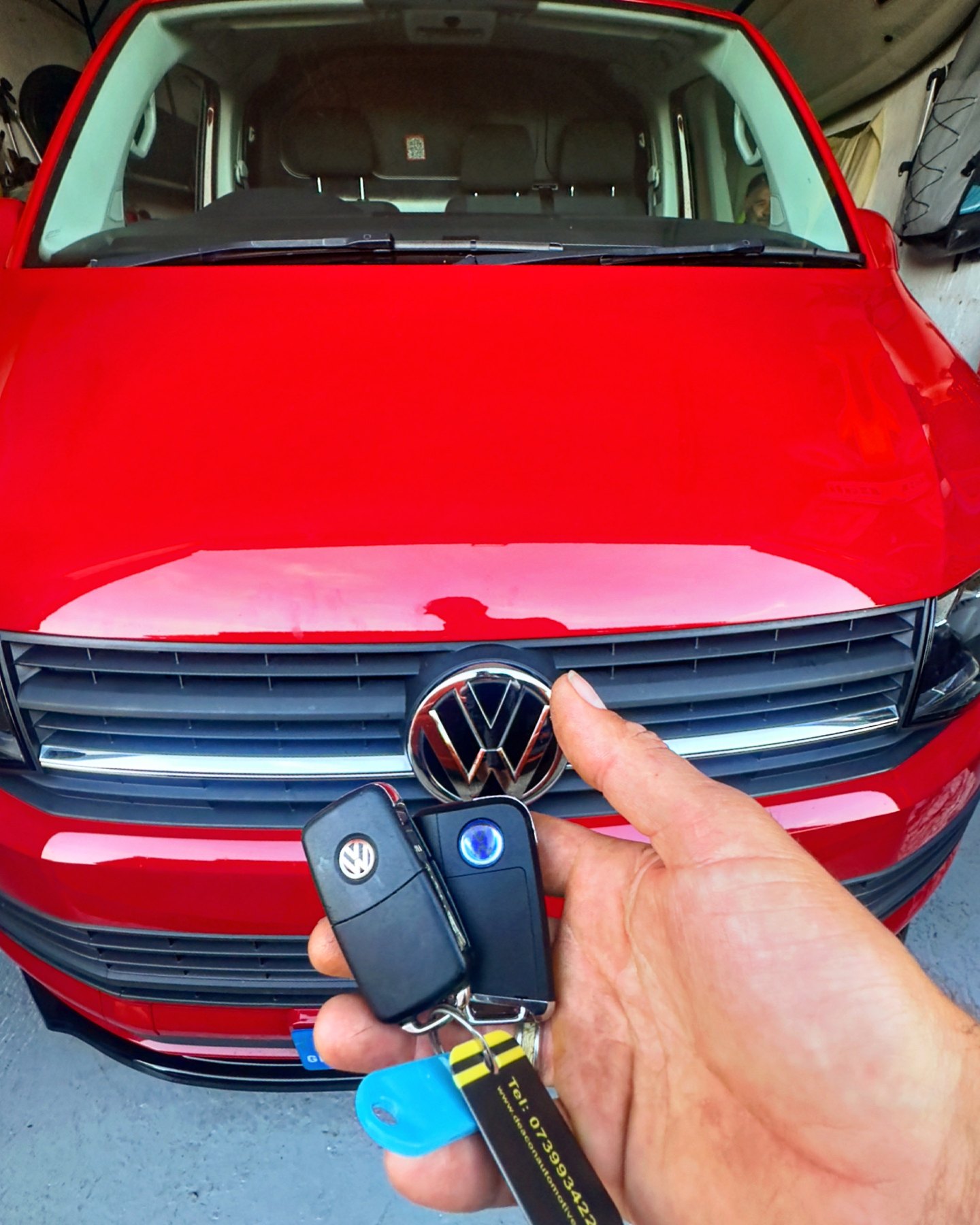 Two Volkswagen remote keys held in front of a red Volkswagen van